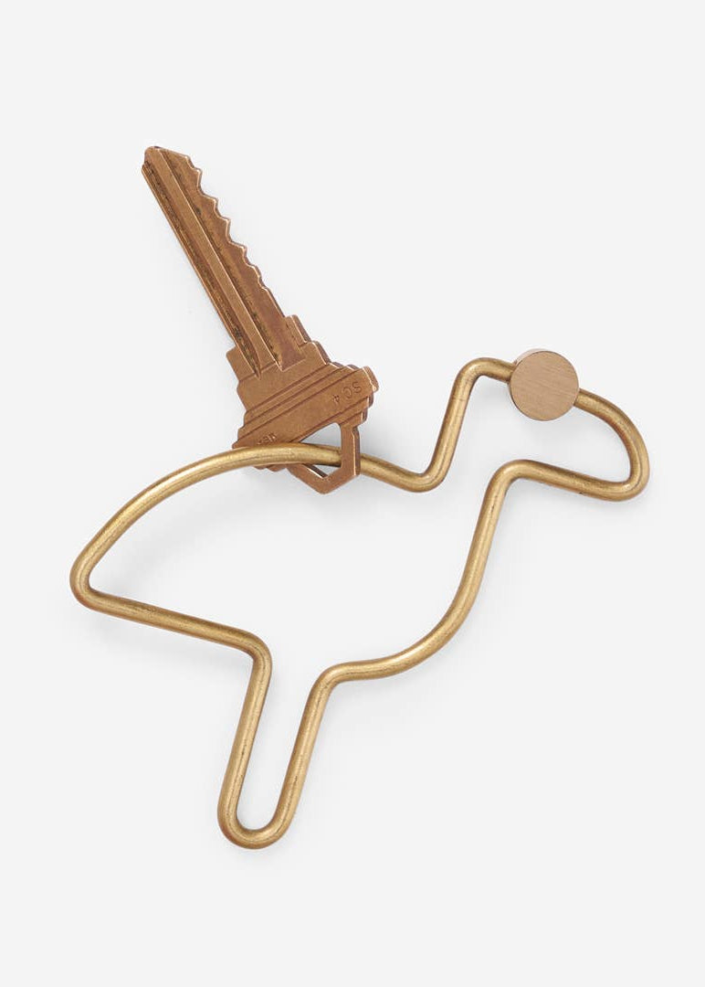 Gold metal key holder shaped like a bird with a key attached on a white background