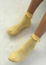 Yellow socks with ruffled top worn by a person on a light gray background