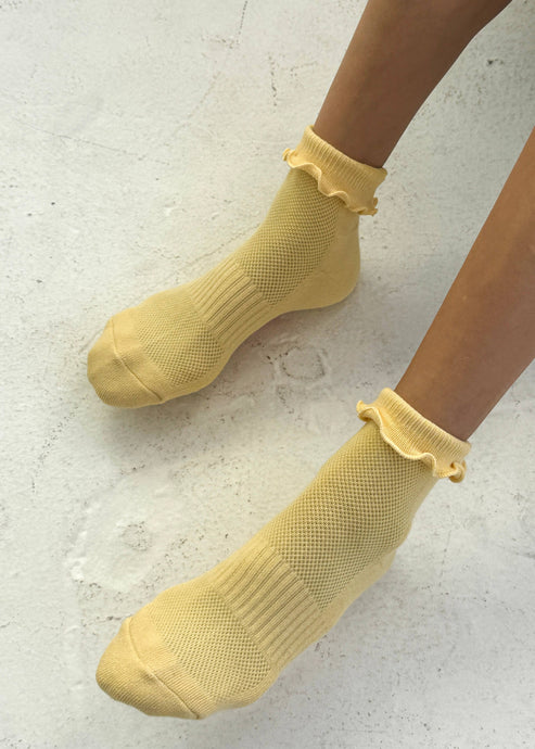 Yellow socks with ruffled top worn by a person on a light gray background